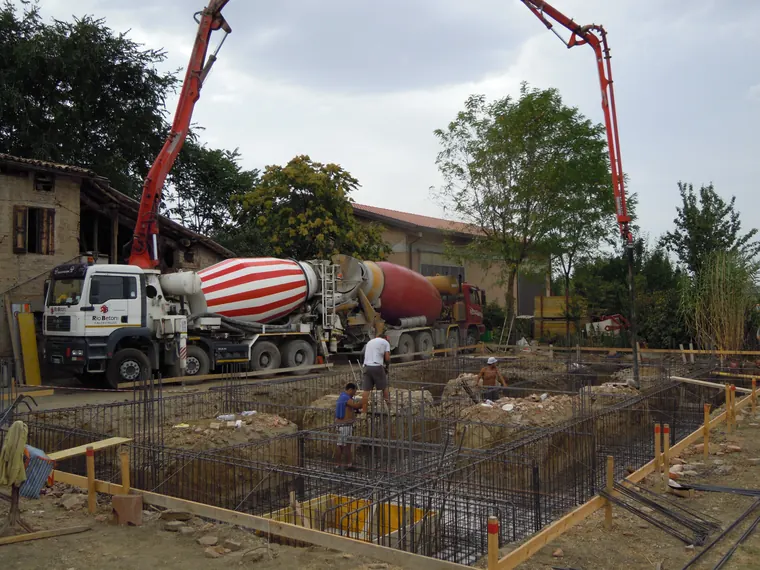 Getto delle fondazioni con betoniera e operatori in cantiere